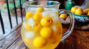 Vaso transparente con agua de nanche, hielos y nanches frescos flotando, sobre mesa rústica. – (Imagen Ilustrativa Infobae)