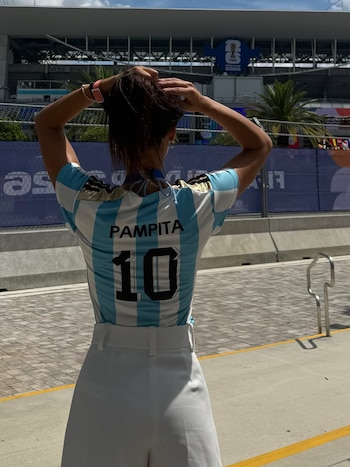 Vista trasera de una mujer con camiseta azul y blanca de Argentina, número 10 y "PAMPITA" en la espalda, recogiendo su cabello frente a un estadio en Miami