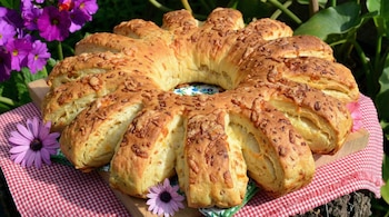 Una cremona de queso parmesano dorada y crujiente, con forma de flor, sobre una tabla de madera y mantel a cuadros, rodeada de flores moradas.