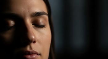 Primer plano de la mitad derecha del rostro de una persona con los ojos cerrados, en un entorno oscuro, con luz sutil resaltando la piel.