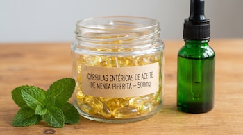 Frasco de vidrio lleno de cápsulas amarillas con etiqueta de papel, hojas de menta verde, botella de vidrio verde con gotero sobre superficie de madera.