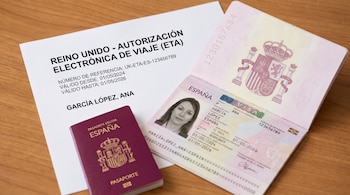 Documento impreso de autorización de viaje británica junto a un pasaporte español abierto con fotografía y otro cerrado sobre una mesa de madera.