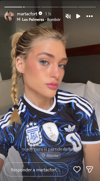 Primer plano de Marta Fort con cabello rubio en trenzas, camiseta negra de la selección argentina, maquillaje azul en ojos y texto que indica "ready para el partido de hoy" en Atlanta