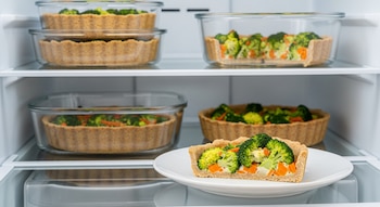 Varias tartas de brócoli y zanahoria con masa integral en recipientes transparentes dentro de una heladera, con una porción en un plato blanco.