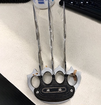 Un puño de metal con tres hojas puntiagudas cubiertas con plástico protector sobre una superficie clara junto a un teclado