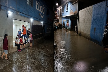 Dos fotografías unidas que muestran una calle nocturna inundada de agua y lodo, con varias personas cerca de edificios de color azul.