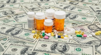 Billetes de cien dólares de Estados Unidos cubren una superficie con cinco frascos de medicamentos y pastillas de distintos colores y tamaños.