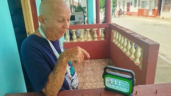 Un hombre mayor señala una lámpara portátil recargable colocada sobre un muro de concreto