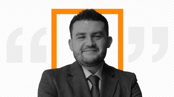 Un hombre sonriente, con barba, traje y corbata, en blanco y negro. Enmarcado por un rectángulo naranja. Fondo blanco con líneas diagonales y grandes comillas.