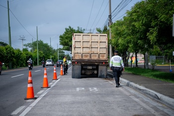 Un gestor de tránsito camina de espaldas hacia la parte trasera de un camión de carga rodeado de conos naranjas de seguridad