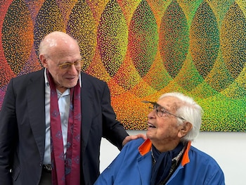 Dos hombres mayores, Julio Crivelli y Julio Le Parc, sonríen frente a una obra de arte abstracto colorida con patrones de puntos