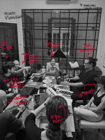 Vista aérea de un grupo de ocho personas, incluyendo Lali Espósito, sentadas alrededor de una mesa larga con laptops en una sala con una pared de cristal