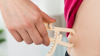 Una mano sostiene un plicómetro de plástico para medir el pliegue de grasa en el abdomen de una persona