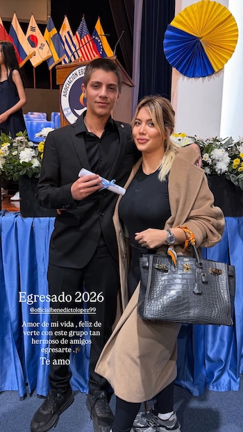 Wanda Nara, con un abrigo beige y un bolso gris, posa junto a su hijo Benedicto, vestido de traje negro y sosteniendo un diploma, en un escenario de graduación