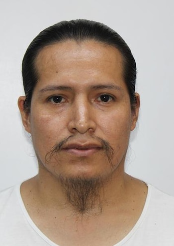 Retrato frontal de un hombre con cabello oscuro recogido, bigote, perilla y camiseta blanca sobre fondo blanco