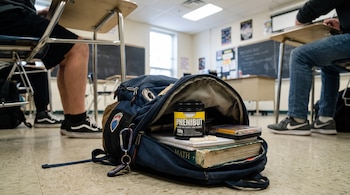 Una mochila azul abierta en el suelo de un aula contiene un frasco marcado como fenibut, cápsulas blancas y libros