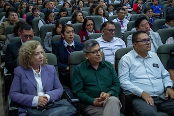 Una audiencia de hombres y mujeres de diversas edades sentados en filas de asientos oscuros dentro de un auditorio. La mayoría mira hacia el frente