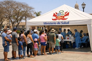 Fila de personas, incluyendo adultos y niños, frente a un puesto de vacunación del Ministerio de Salud de Perú en una plaza.