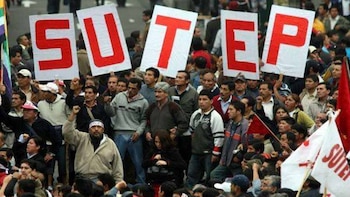 Una multitud reunida en la calle porta pancartas con letras rojas que forman la palabra SUTEP y varias banderas