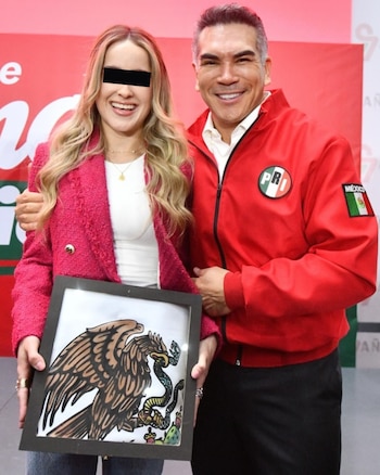 Una mujer con chaqueta fucsia sostiene un cuadro del escudo de México al lado de un hombre vestido con una chaqueta roja que lleva el logotipo del PRI