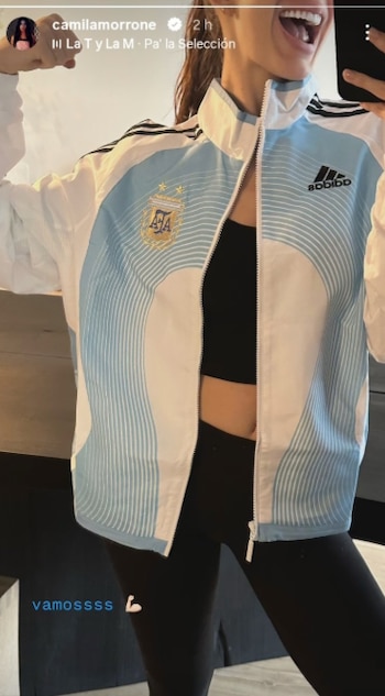 Una mujer toma una selfie vistiendo una chaqueta de la Selección Argentina de fútbol de color blanco y celeste, un corpiño deportivo negro y calzas negras