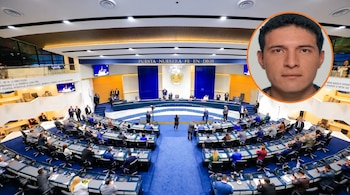 Fotografía aérea de la Asamblea Legislativa de El Salvador en sesión, mostrando a diputados y personal, con un retrato de un hombre en un círculo superior derecho.