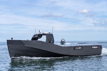Buque gris oscuro con matrícula 1-YJ-874 y el nombre 'FENDER-2' en su costado, navegando en el mar, con un segundo barco similar detrás