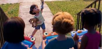 Una niña levanta un muñeco de Woody y sostiene un muñeco de caballo, Bullseye. Tres niños de espaldas observan a la niña en una acera con césped