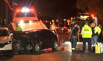 Un automóvil negro destruido en la parte frontal junto a socorristas con chalecos reflectantes y grúas con luces encendidas