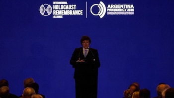 Javier Milei, con traje oscuro y corbata clara, habla en un podio negro ante un fondo azul con los logos de la IHRA y Argentina Presidencia 2026