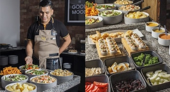 Un empleado sonriente con delantal negro y beige atiende un extenso buffet con ensaladas, sushi, verduras, quesos y otros platillos frescos en The House Restaurante