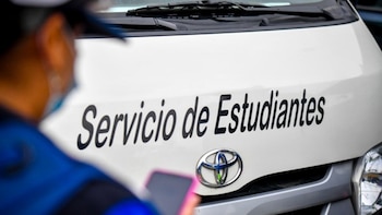 Parte frontal de un vehículo blanco con la inscripción Servicio de Estudiantes junto a una persona con chaleco azul