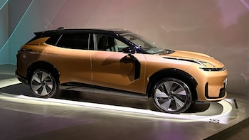 Un automóvil SUV color bronce con techo negro, vidrios oscuros, y llantas de diseño complejo, expuesto sobre una plataforma iluminada