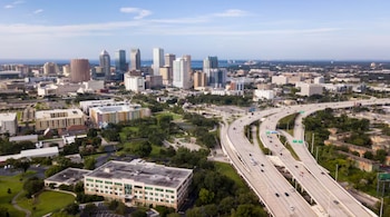 Vista aérea de la ciudad de Tampa con rascacielos, edificios residenciales, un complejo cruce de autopistas con tráfico y áreas verdes bajo un cielo azul claro