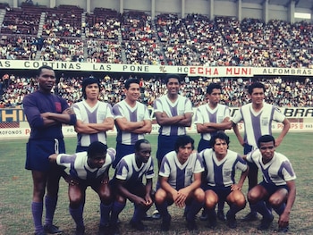Once futbolistas con uniforme a rayas moradas y blancas posan de pie y en cuclillas sobre el césped ante una tribuna con público