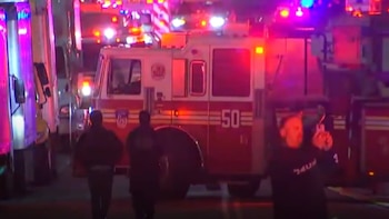 Camión de bomberos blanco y rojo con el número 50, luces de emergencia rojas y azules intermitentes en la oscuridad, y siluetas de personas al frente