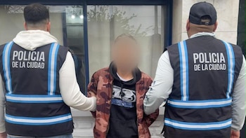 Dos agentes de la Policía de la Ciudad sujetan de los brazos a un hombre con el rostro difuminado frente a un edificio