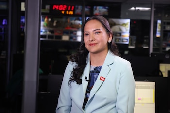 Cinthia Ramírez Santillana, con blazer celeste y pin de IRTP, sonríe en una sala de control de televisión, con múltiples monitores y un reloj digital visible al fondo