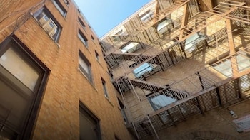 Edificio de ladrillo con numerosas ventanas y escaleras de incendio metálicas, visto desde abajo contra un cielo azul claro