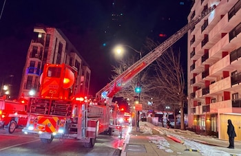Un camión de bomberos estacionado de noche en una calle con nieve extiende una escalera de rescate hacia la fachada de un edificio