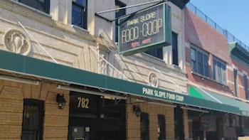 Fachada de un edificio de ladrillo con un letrero que dice "Park Slope Food Co-op", un toldo verde, ventanas y el número "782" sobre una entrada oscura