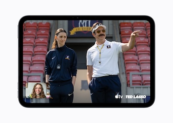 Tableta iPad mini que muestra en pantalla a dos personas con ropa deportiva en un estadio y una videollamada en la esquina inferior izquierda