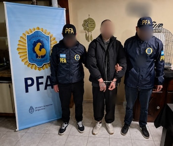Dos agentes de policía con uniforme de la PFA y gorras PFA escoltan a un hombre esposado frente a un banner de la Policía Federal Argentina
