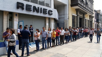 Larga fila de personas en la acera frente al edificio de RENIEC. Ciudadanos esperan en la calle mientras otros transitan; algunos sostienen documentos de identidad.