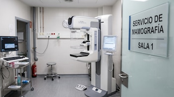 Un mamógrafo en el centro de un consultorio médico con una puerta de vidrio que tiene la señalización Servicio de mamografía Sala 1.