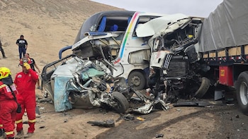Vehículos destruidos tras una colisión en una carretera junto a un cerro árido, con un bombero con traje rojo en primer plano