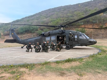 Seis uniformados de la policía permanecen arrodillados en un helipuerto frente a un helicóptero militar con una colina al fondo