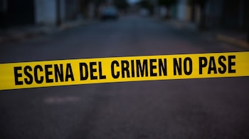 Cinta amarilla con la frase 'ESCENA DEL CRIMEN NO PASE' en letras negras, estirada horizontalmente frente a una calle borrosa y oscura.