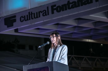 Una mujer con gafas y abrigo claro habla frente a un micrófono desde un podio, bajo un letrero que dice cultural Fontanarrosa