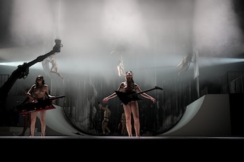 Múltiples figuras semidesnudas en un escenario cubierto de niebla, con dos en primer plano sosteniendo guitarras eléctricas y otras suspendidas